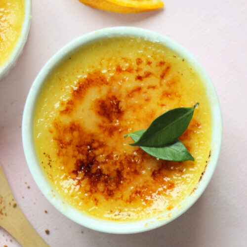 White ramekin with creme brulee. Orange slices on the side.