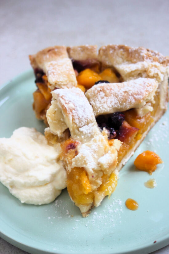 Peach pie portion with whipped cream on an aqua-green plate.