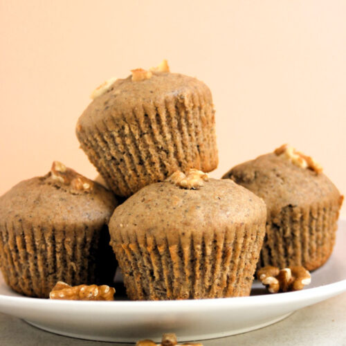 Many banana muffins on a white plate and walnuts scattered around.