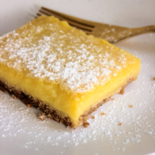 Lemon bar sprinkled with powdered sugar on a white plate.