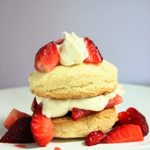 Strawberry shortcake on a white plate and strawberries on the sides.