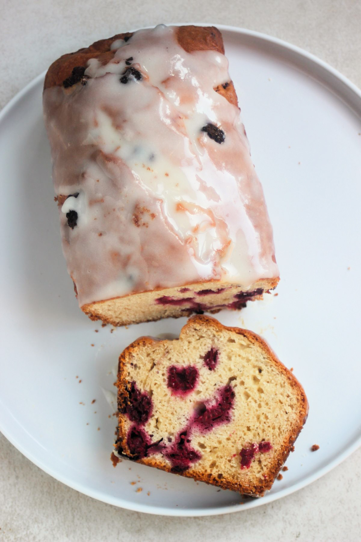 Raspberry loaf cake with icing and a cut portion of it on a white plate seen from above.