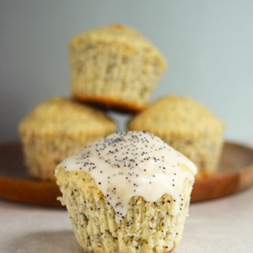 Lemon muffin with icing and poppy seeds. More muffins behind.