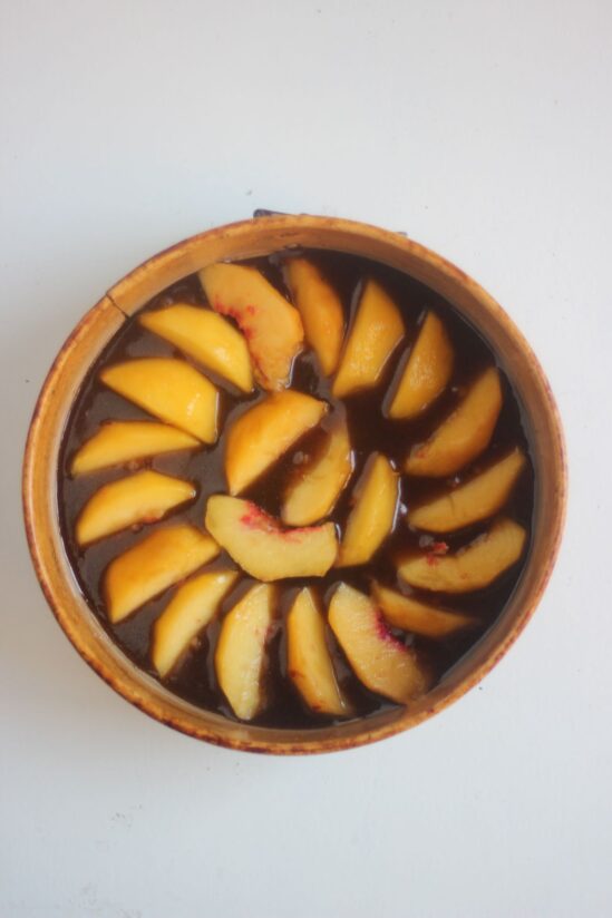 Round cake pan with caramel and sliced peaches seen from above.