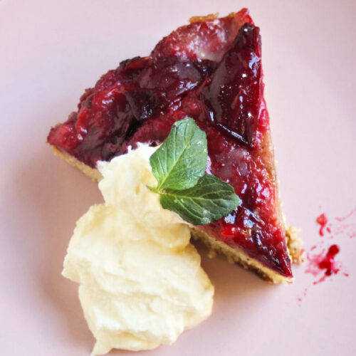 Portion of plum upside down cake and whipped cream on a pink plate.