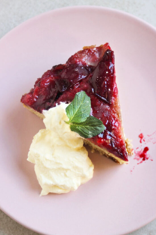 Portion of plum upside down cake and whipped cream on a pink plate.