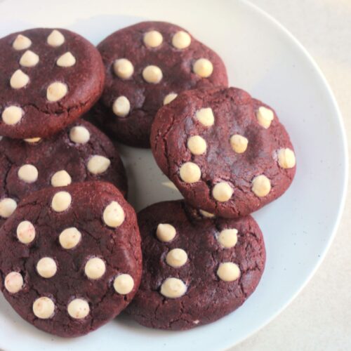 Red velvet cookies with white chocolate chips on a white plate.