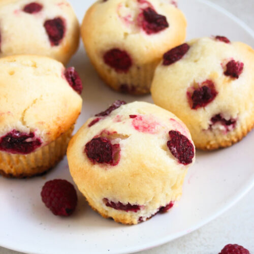 Raspberrie muffins and fresh raspberries on a white plate.