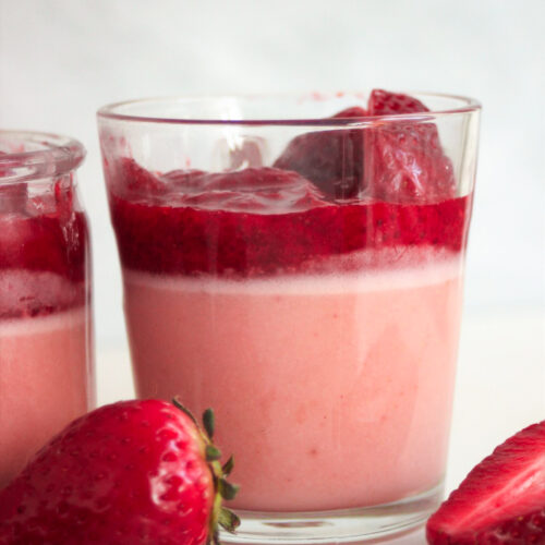 Glass cup with strawberry panna cotta and strawberry sauce. Fresh strawberries on the side.