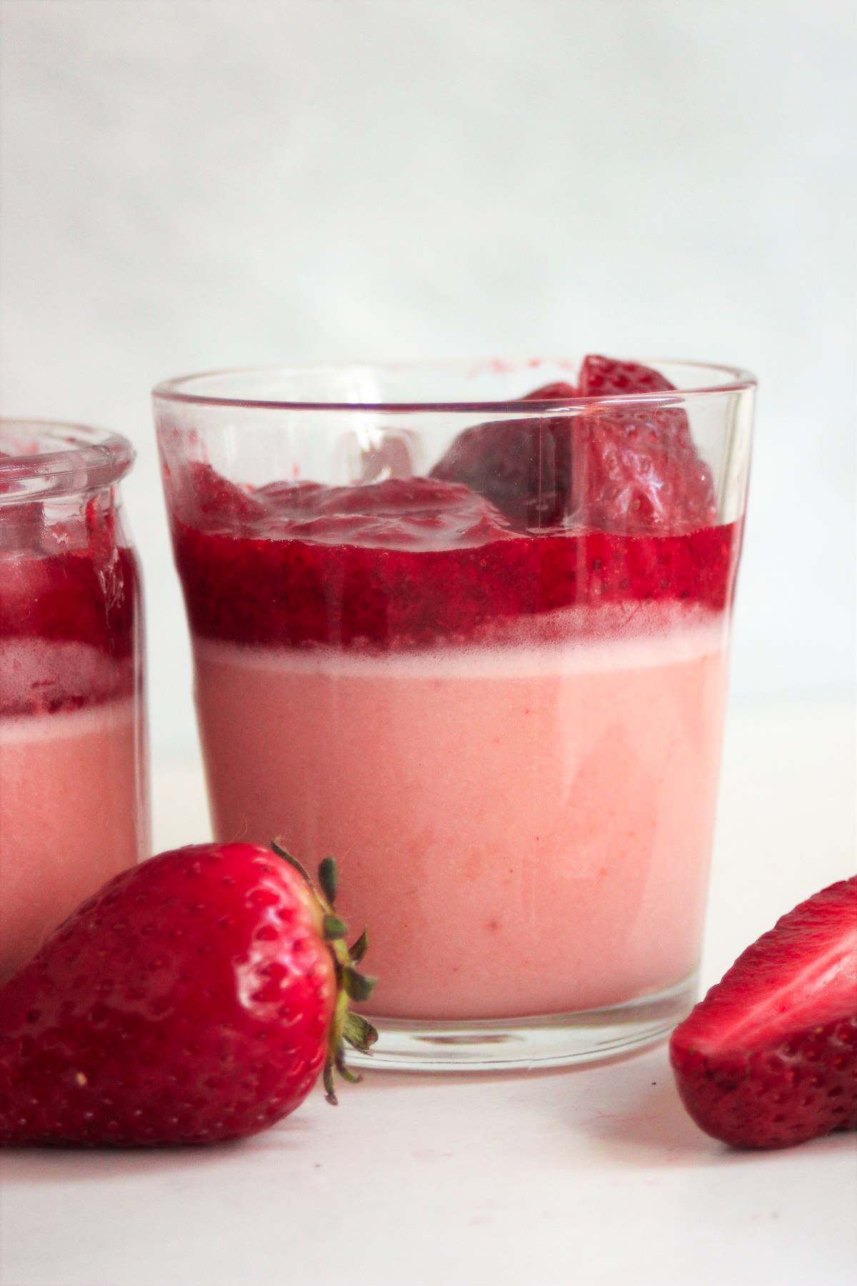 Glass cup with strawberry panna cotta and strawberry sauce. Fresh strawberries on the side.