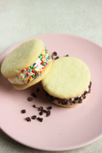 Two ice cream cookie sandwich , one leaning on the other, and cocoa nibs on a pink plate.