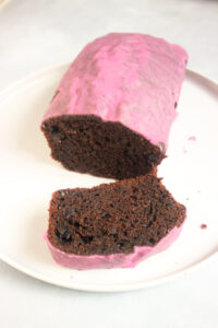 Chocolate beet loaf cake with pink icing and a cutten slice of it on a white plate.
