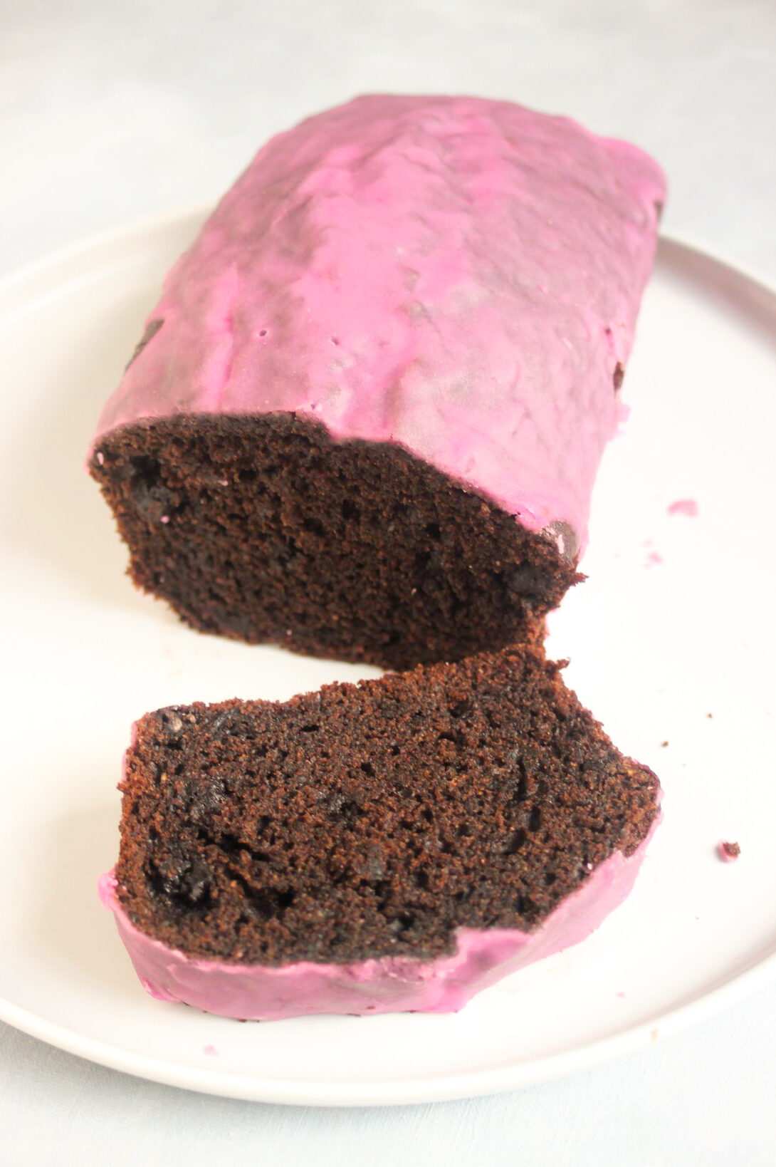 Chocolate beet loaf cake with pink icing and a cutten slice of it on a white plate.