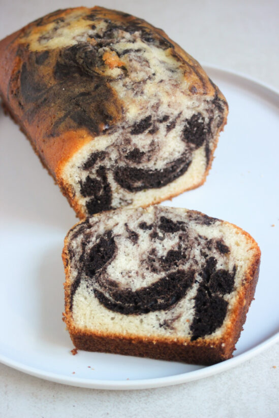 Marble loaf cake and a slice of it on a white plate.
