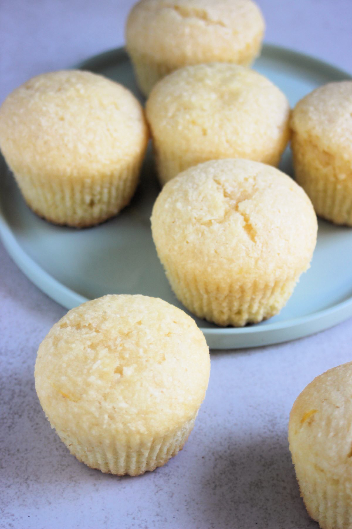 Orange coconut muffins on a white surface and more behind on an aqua-green plate.