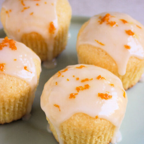 Orange coconut muffins with icing on an aqua-green plate.