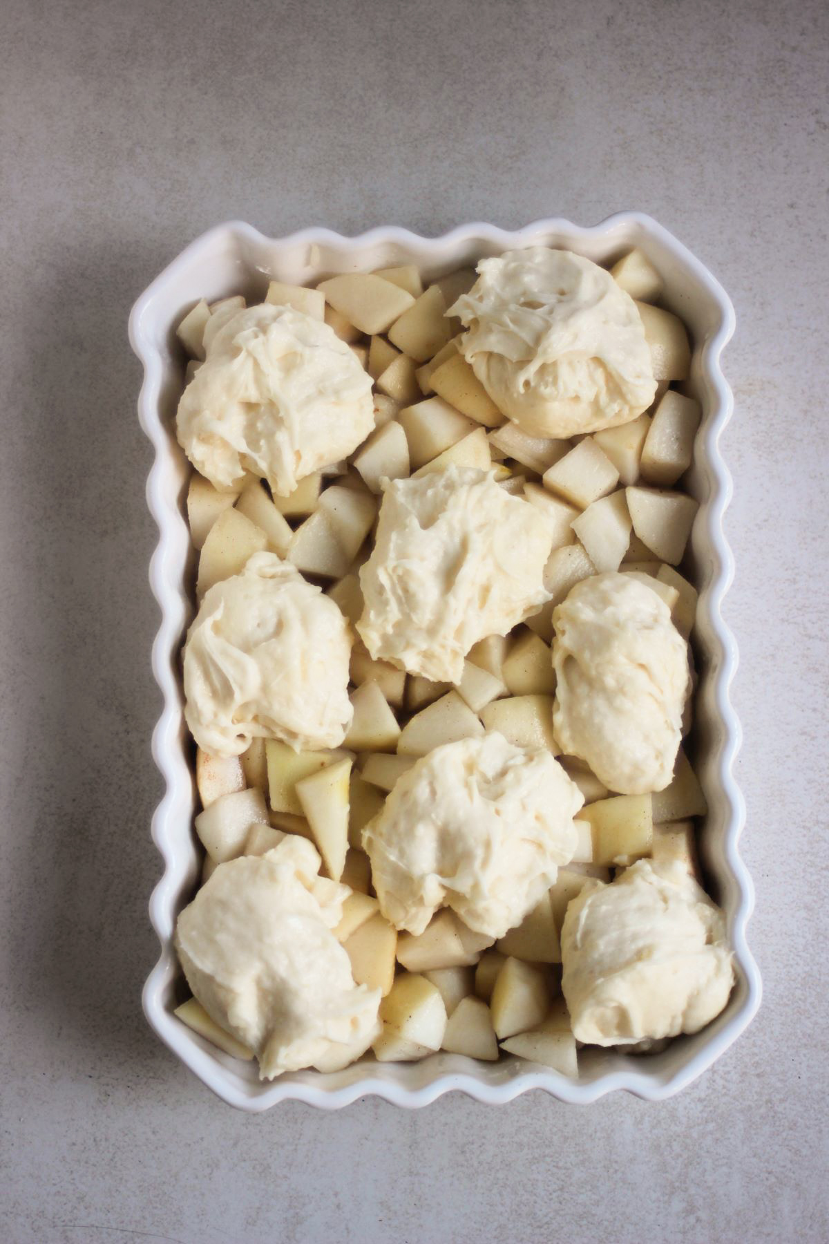 Rectangular white baking dish with chopped pears and scoop of dough.