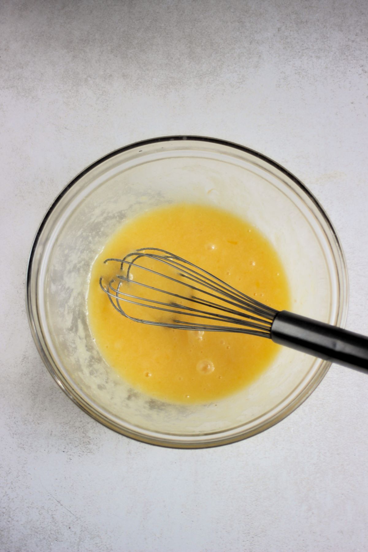 Glass bowl with a yellow mixture and a hand whisk.