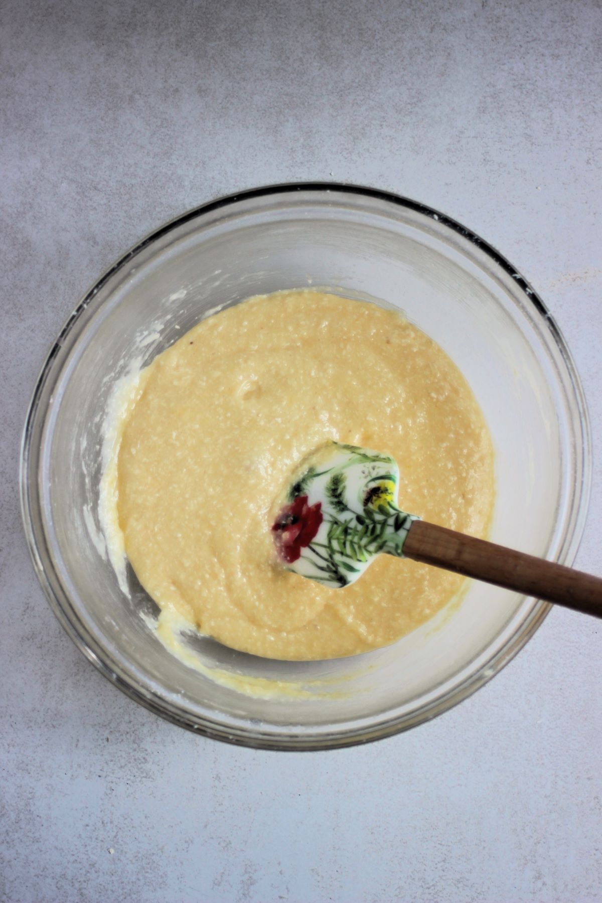 Glass bowl with a cream colour mixture and a rubber spatula.