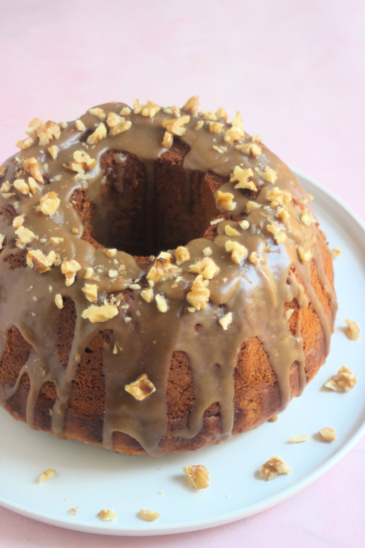 Banana bundt cake with brown sugar icing and walnuts on a white plate. Pink surface.