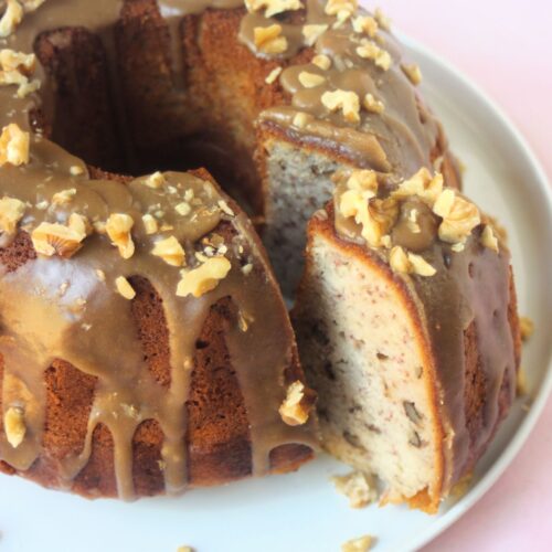 Banana cake with brown sugar and walnut icing on a white plate, with a slice of the cake cut out.