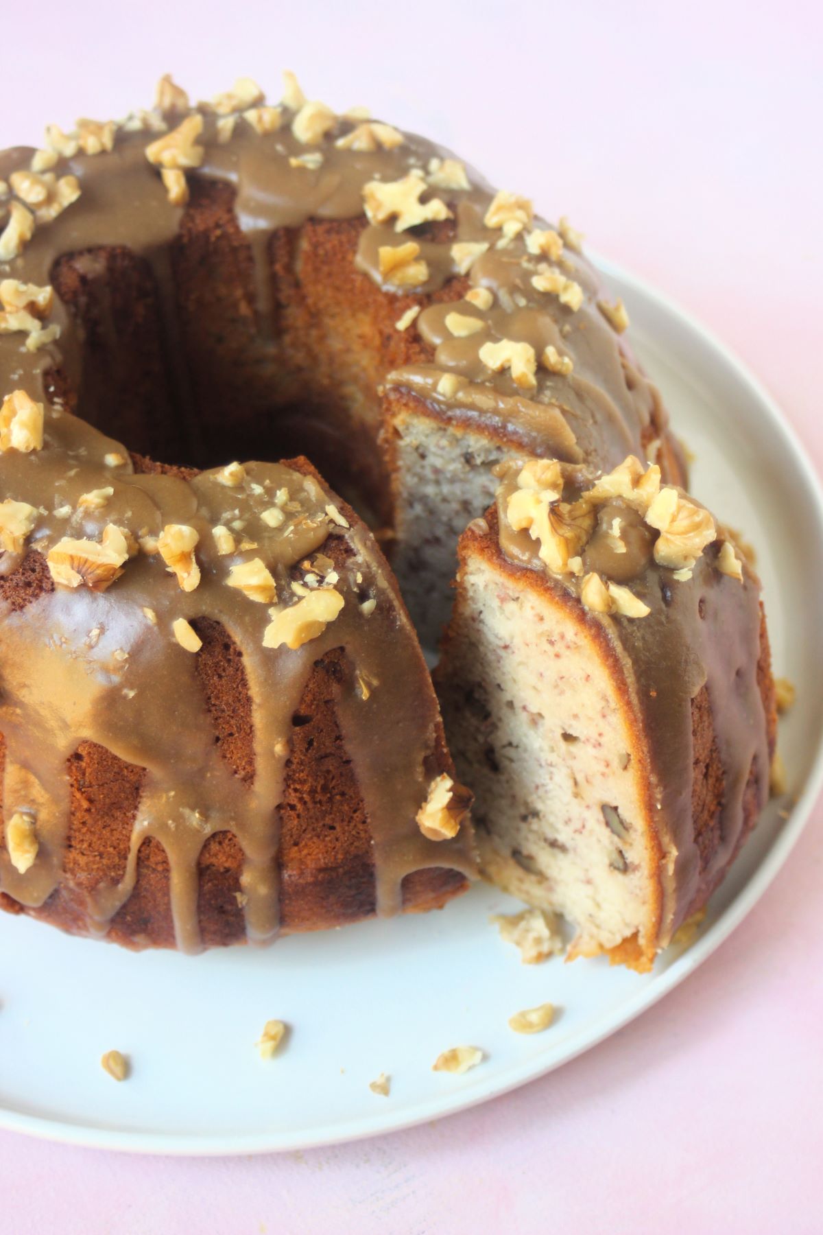 Banana cake with brown sugar and walnut icing on a white plate, with a slice of the cake cut out.