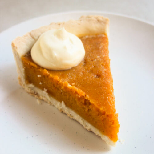 Portion of pumpkin pie en a scoop of whipped cream on a white plate.