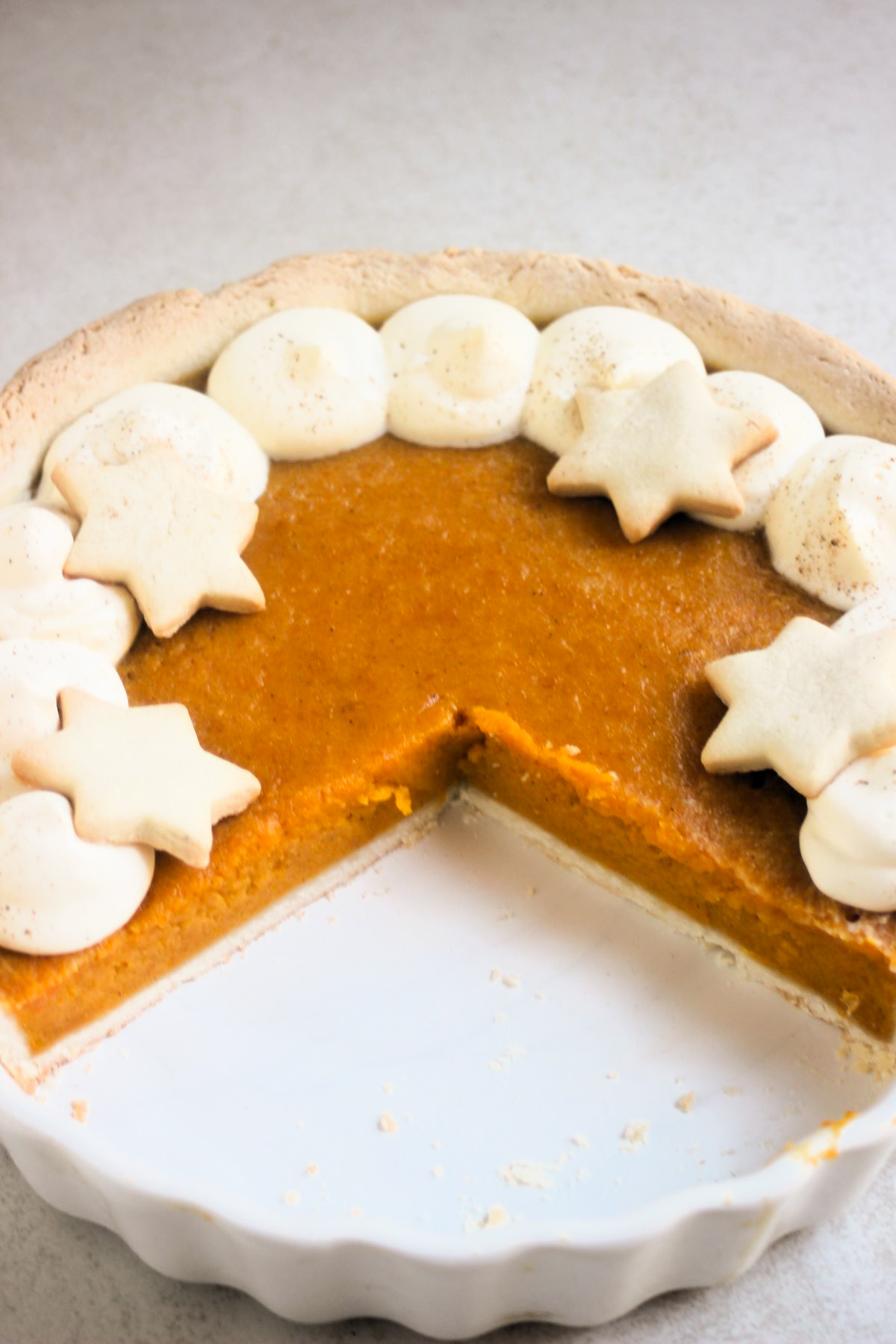 Three-quarters of a pumpkin pie with whipped cream and star-shaped cookies on a round ceramic baking dish.