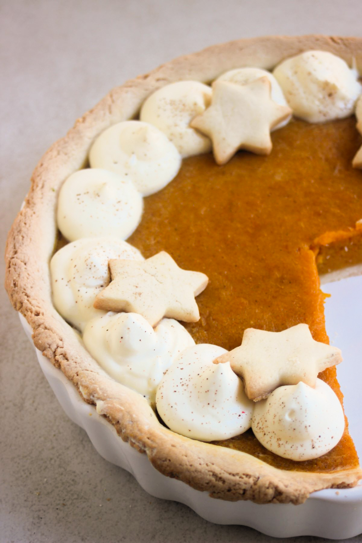 Pumpkin pie with whipped cream and star-shaped cookies on a round ceramic baking dish.