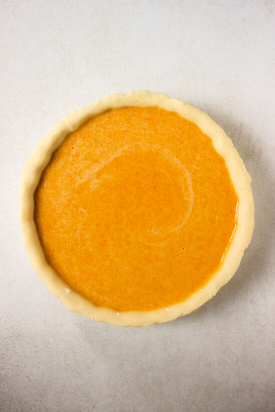 Raw pumpkin pie on a white surface seen from above.