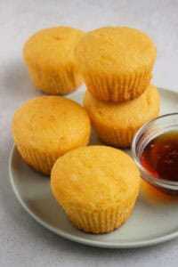 Cornbread muffins and a dip of honey on an aqua-green plate. One muffin is stack on another muffin.