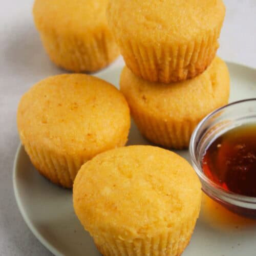 Cornbread muffins and a dip of honey on an aqua-green plate. One muffin is stack on another muffin.