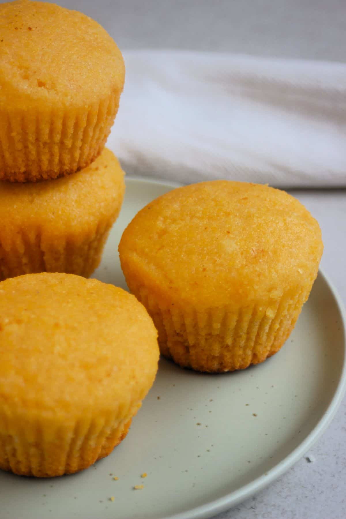 Cornbread muffins, one is stack on other muffin, on an aqua-green plate.