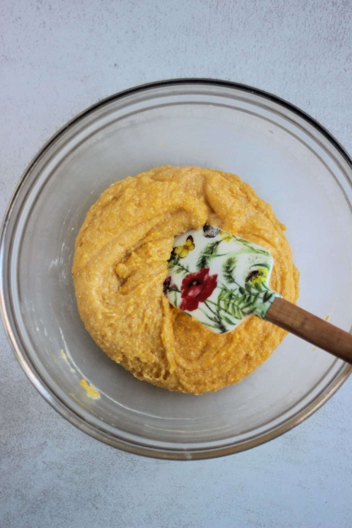 Glass bowl with a yellow mixture and a rubber spatula.