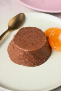 Chocolate panna cotta on an aqua-green colour plate, two fresh tangerine slices and golden spoon.