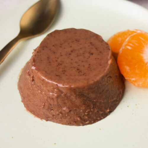 Chocolate panna cotta on an aqua-green colour plate, two fresh tangerine slices and golden spoon.