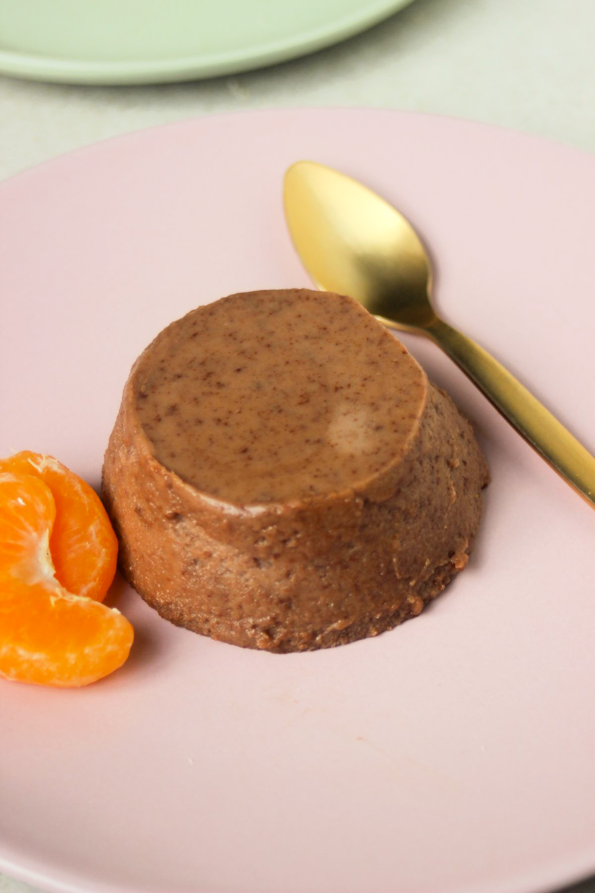 Chocolate panna cotta on a pink plate, two fresh tangerine slices and golden spoon.