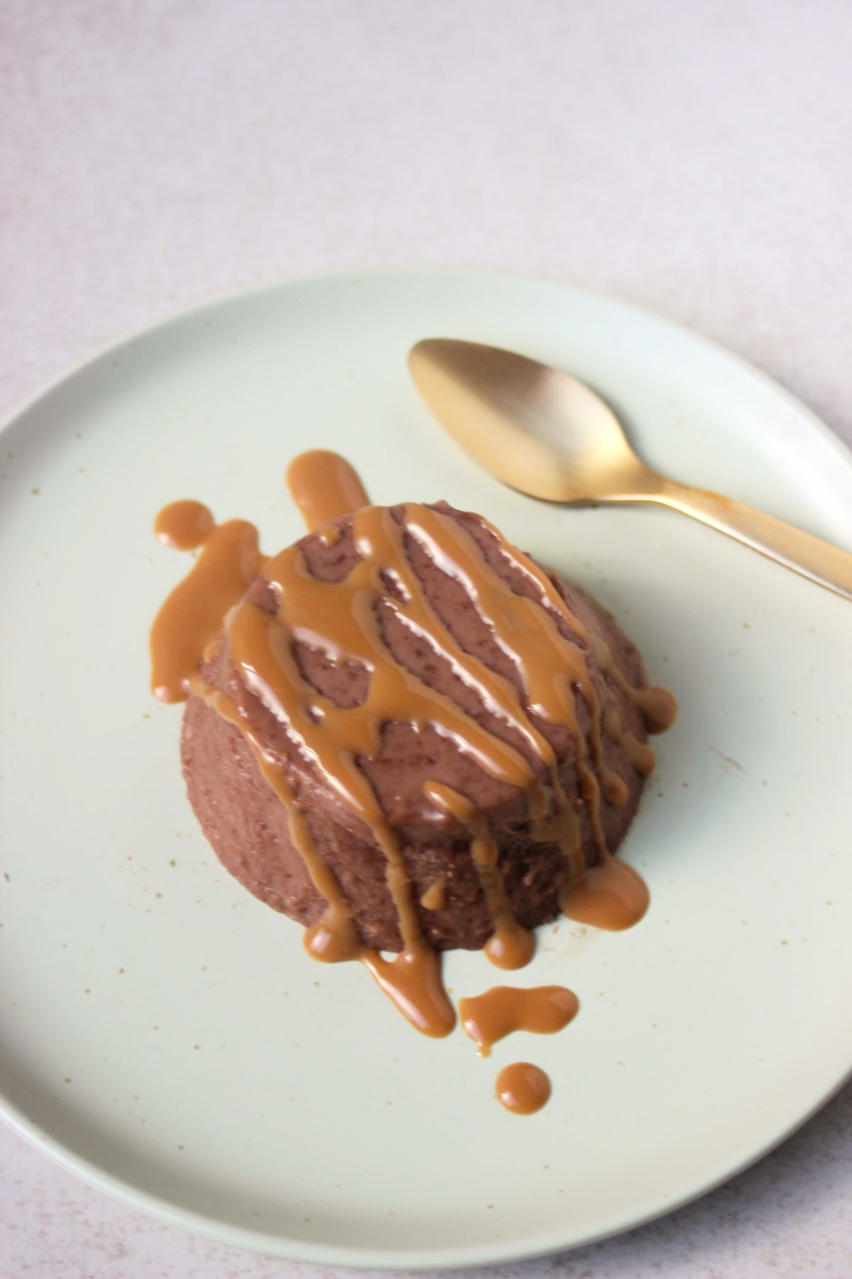 Chocolate panna cotta drizzled with caramel sauce on an aqua-green colour plate and golden spoon.