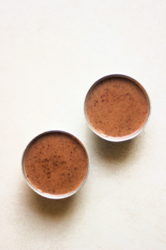 Two stainless ramekins with raw panna cotta seen from above.