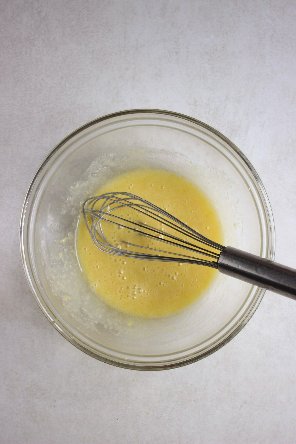Glass bowl with a yellow liquid and a hand whisk.