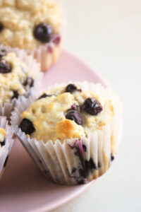 Blueberry muffin with a liner on a pink plate.