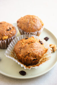 Morning glory muffins on a open liner on a plate. Two muffins behind.