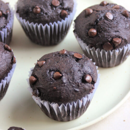 Double chocolate chip muffins with liners on an aqua green plate.