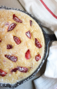 Strawberry clafoutis in a black skillet and a white napkin on the pan handle seen from above.