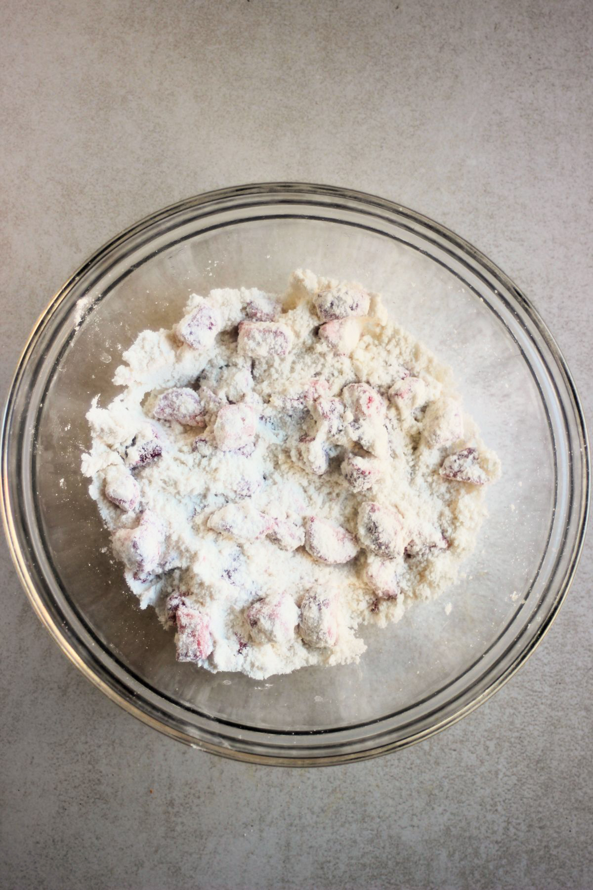 Glass bowl with a mixture that includes GF all-purpose flour and coated strawberries.