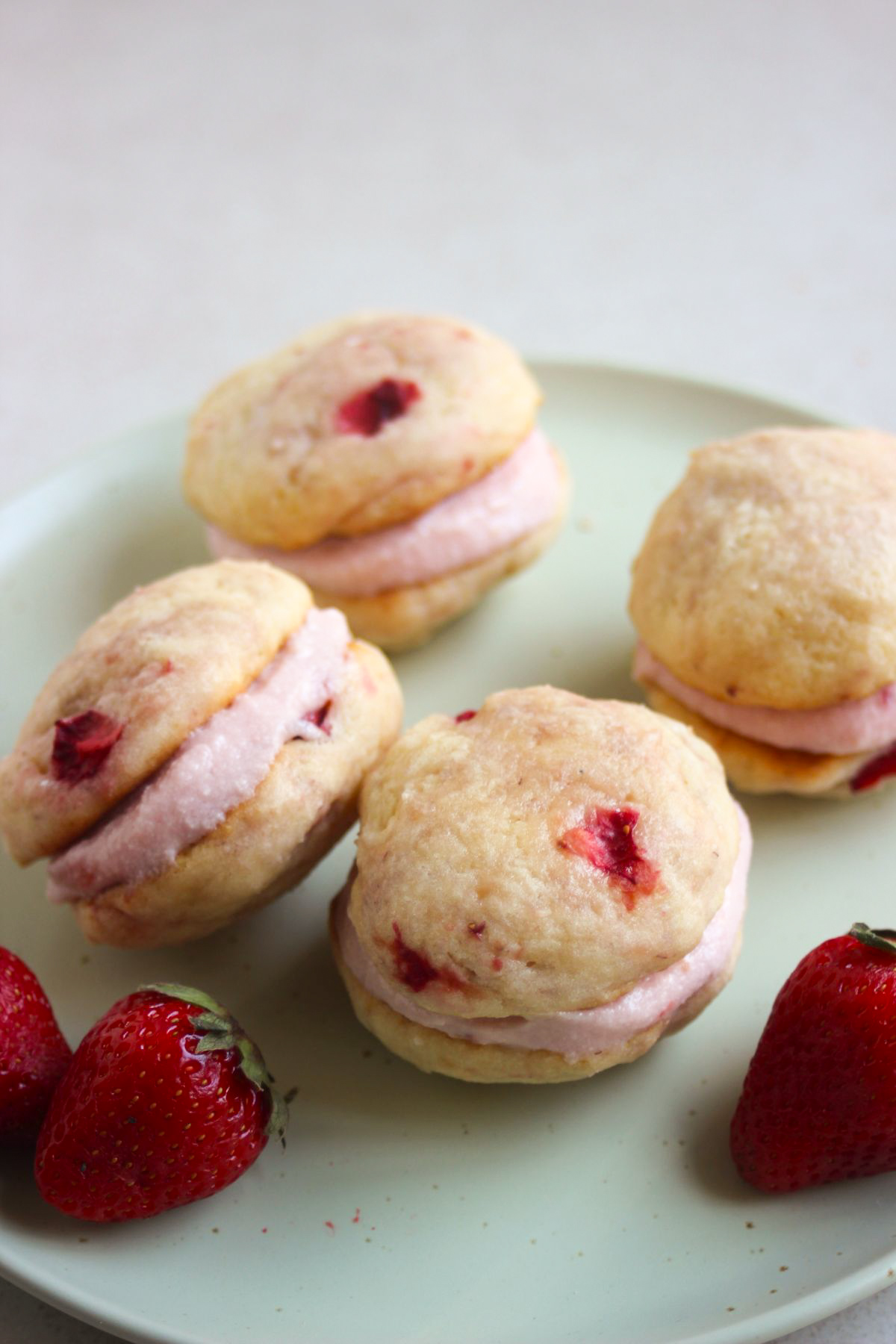 Strawberry whoopie pies and fresh strawberries on an aqua green plate.