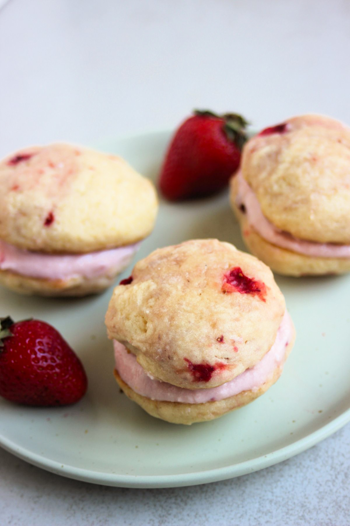 Strawberry whoopie pies and fresh strawberries on an aqua green plate.