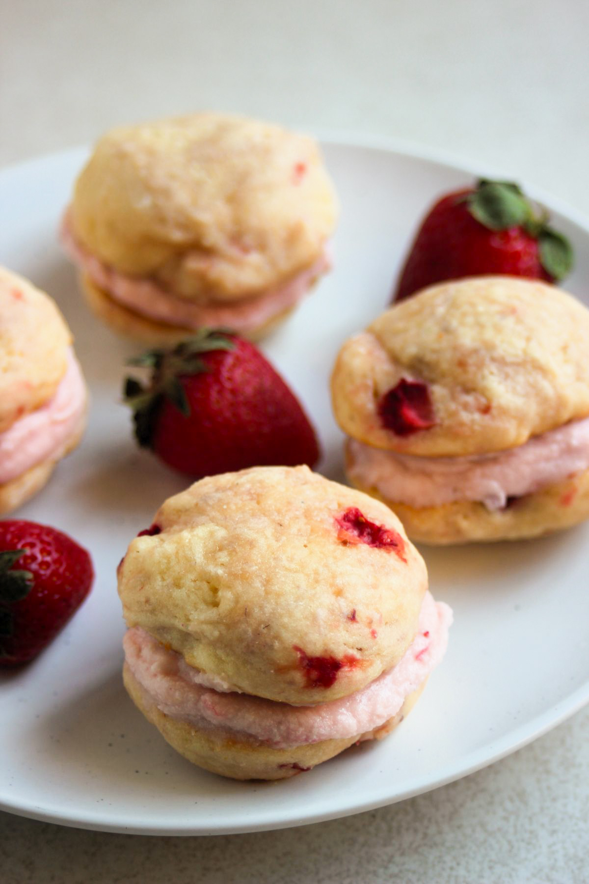 Strawberry whoopie pies and fresh strawberries on a white plate.