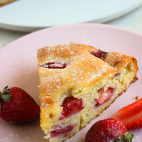 Portion of strawberry cake on a pink plate. Fresh strawberries on the sides.