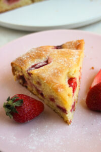 Portion of strawberry cake on a pink plate. Fresh strawberries on the sides.